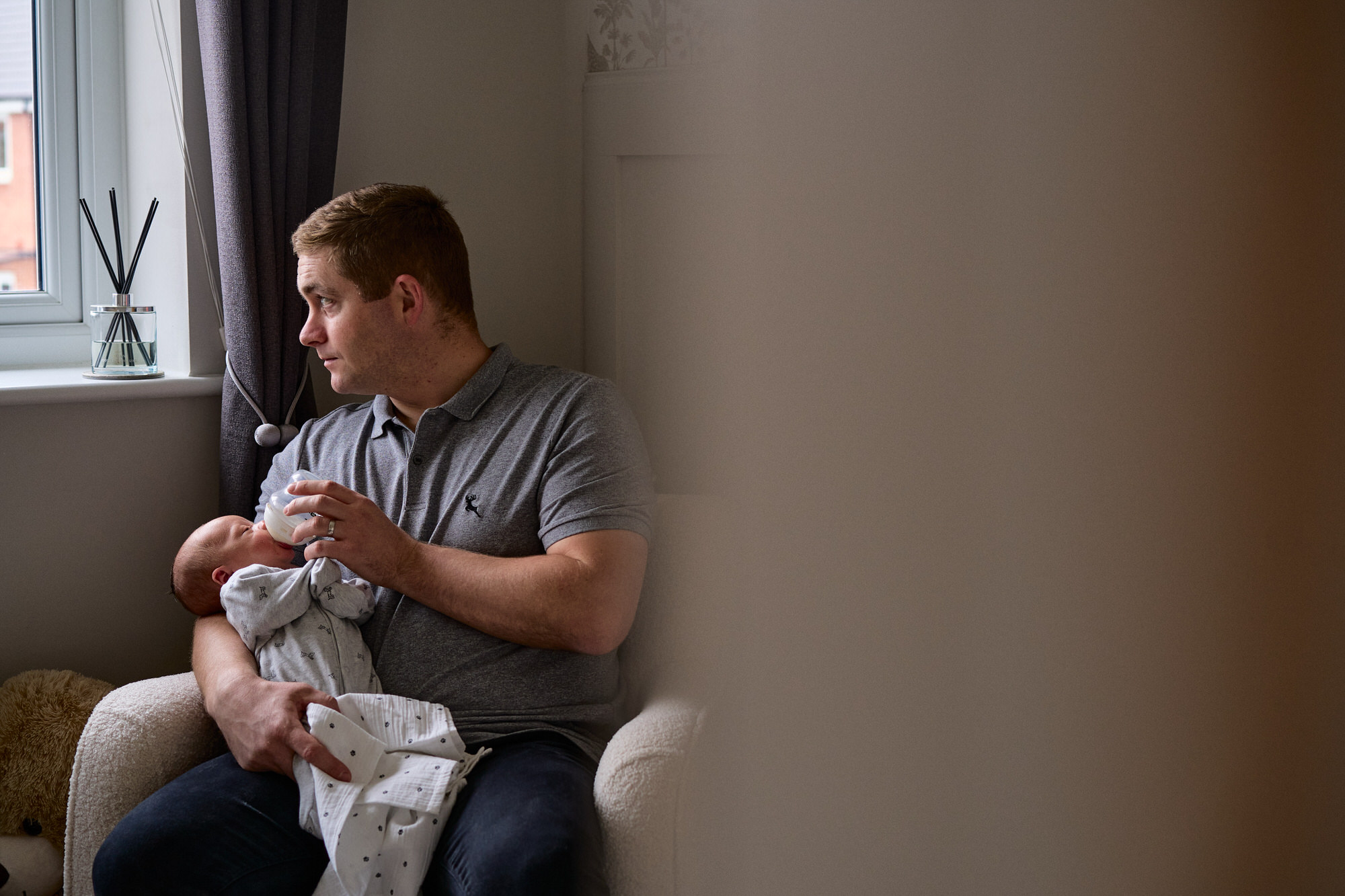 a dad sits on the nursery chair feeding his newborn baby in Warrington