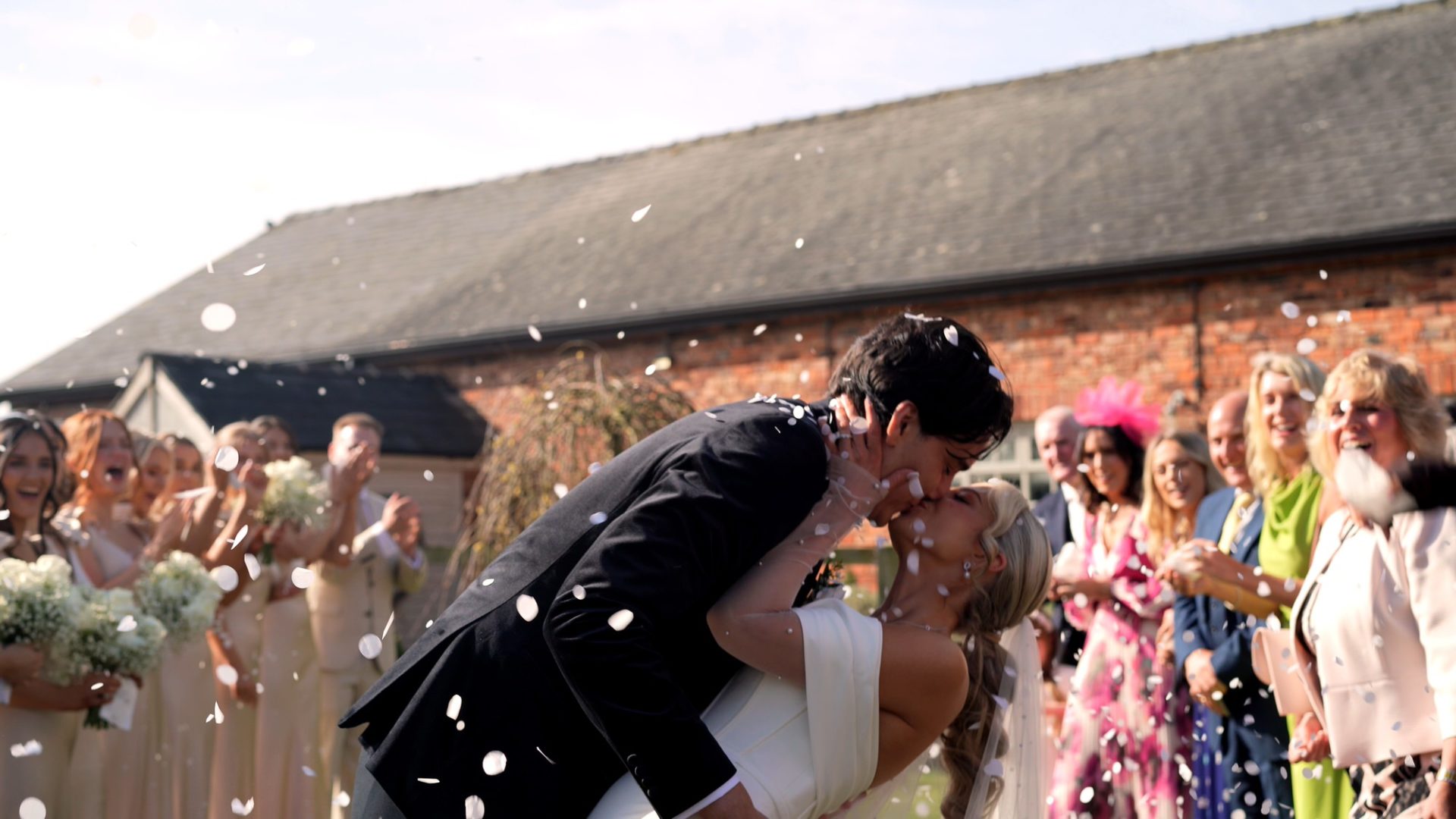 a couple kiss whilst being covered in confetti outside Larkspur Lodge in Cheshire