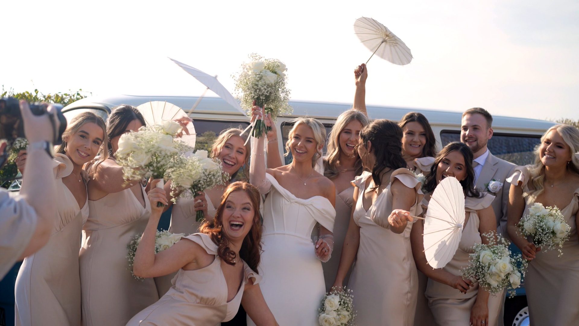 the bride and bridesmaids pose outside the vintage campervan with parasols