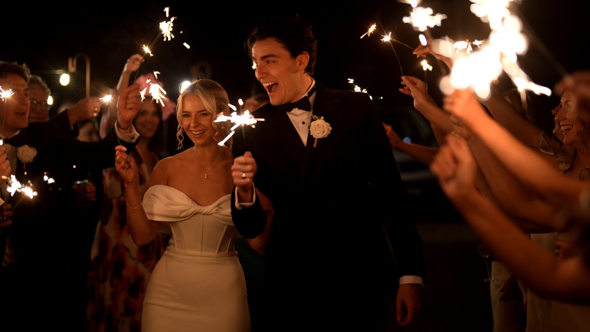 a couple in black tie laugh during a sparkler walk outside Larkspur Lodge in Cheshire