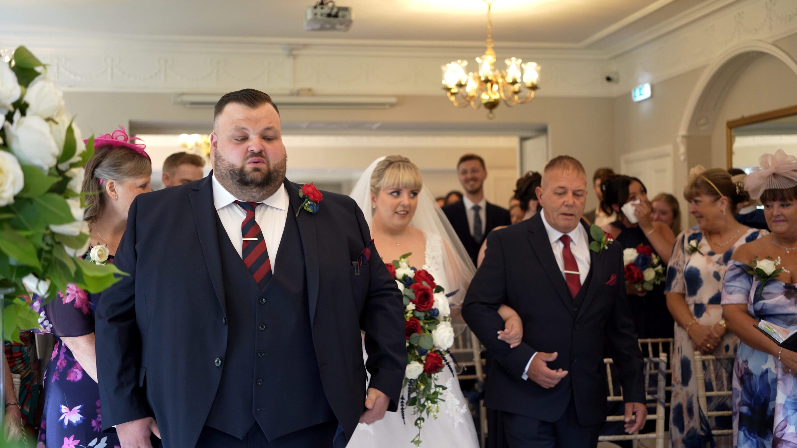 an emotional groom takes a deep breath as his bride is walked down the aisle on the arm of her dad