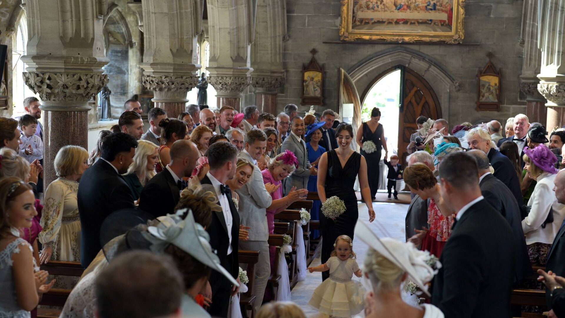 a chapel full of wedding guests watch the bridesmaids walk down the aisle