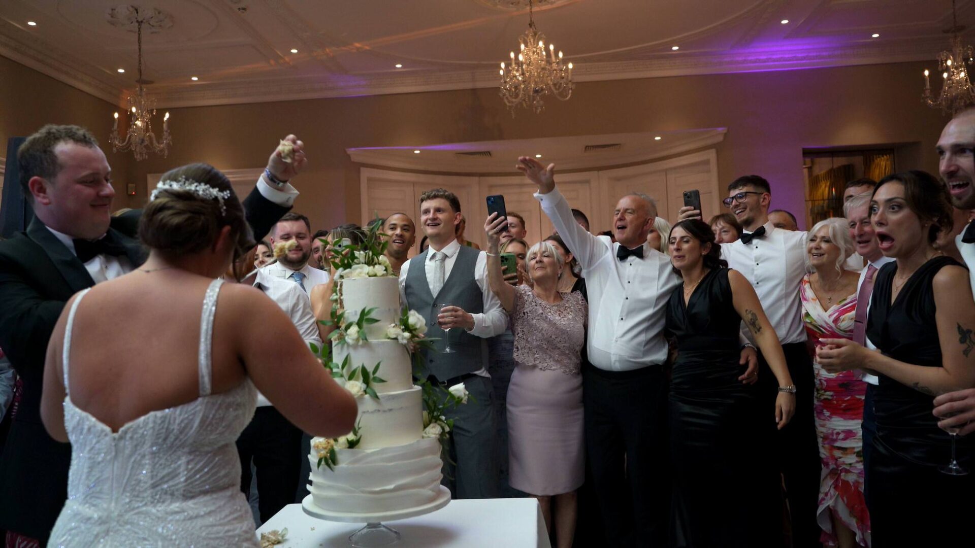 fun reactions and guests cheer as the Groom holds up a piece of cake